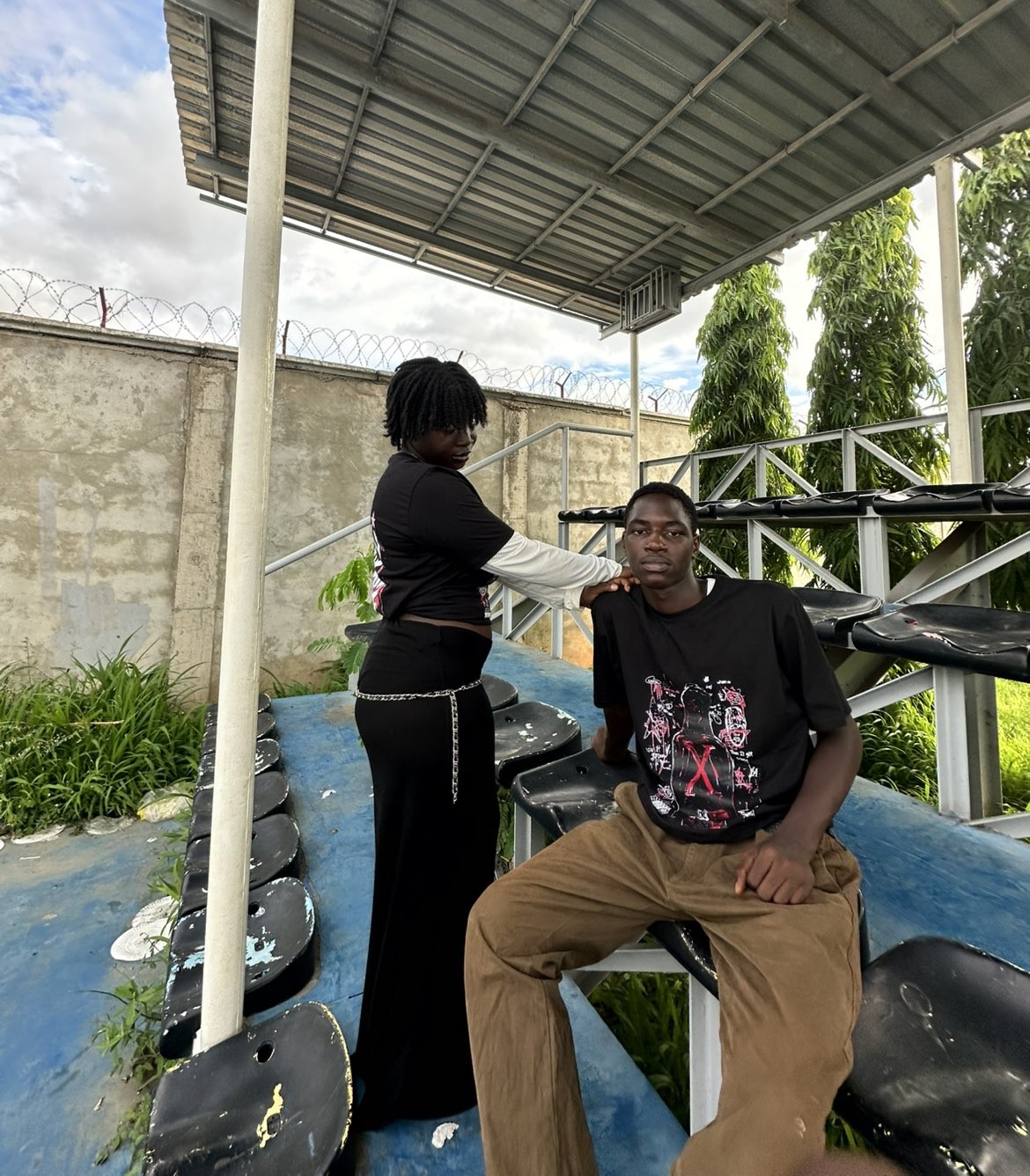 Fresh Universe streetwear models posing under stadium bleachers, featuring a female model resting her hand on a male model wearing a black graphic tee.
